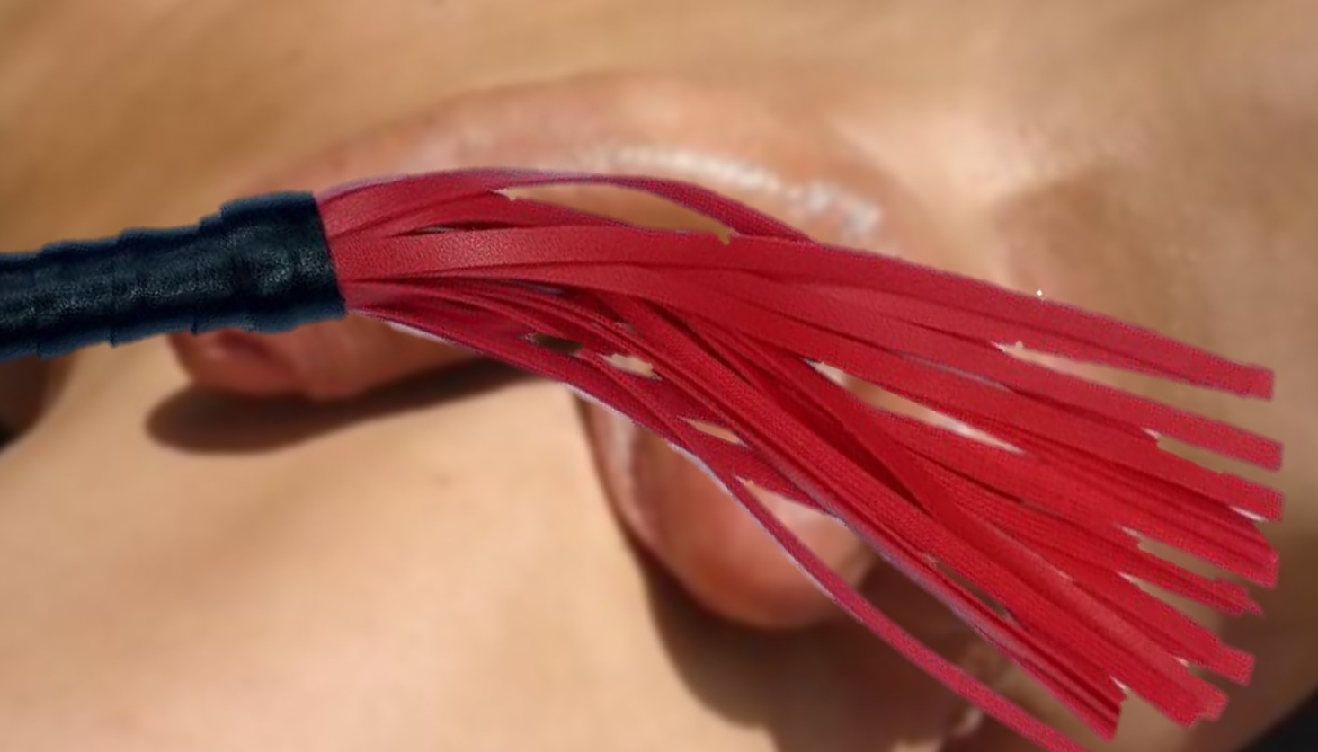 Yvonne drags the red tails of her flogger across a man's cock and balls. What a tease she is!